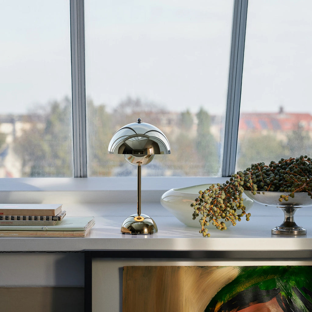 Modern desk lamp on a desk with a cityscape view through large windows.