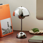 Modern silver table lamp on a wooden surface with books and decorative items.