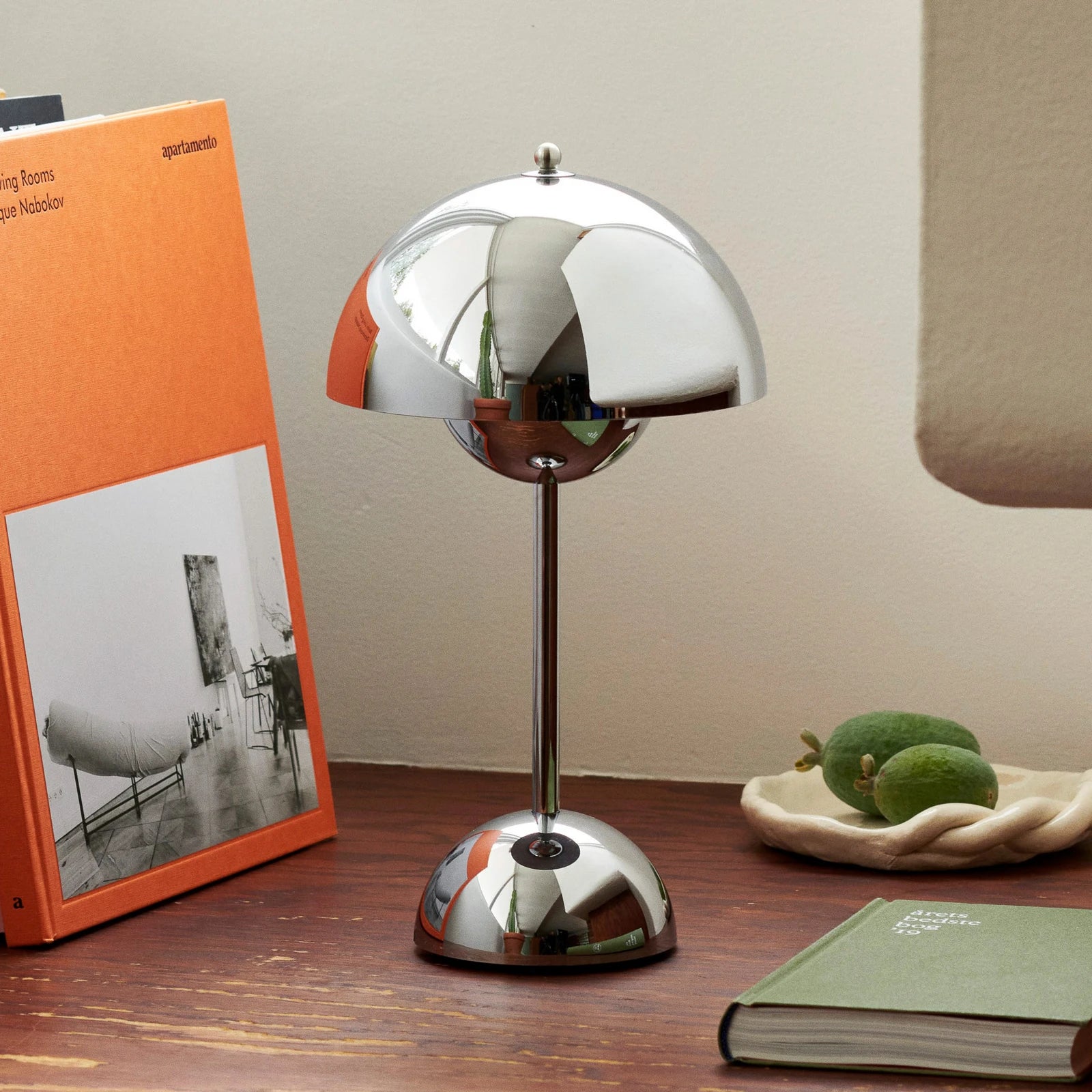 Modern silver table lamp on a wooden surface with books and decorative items.