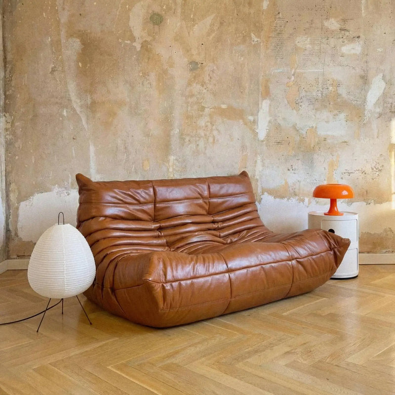 Brown leather sofa in a room with a textured wall and wooden floor.